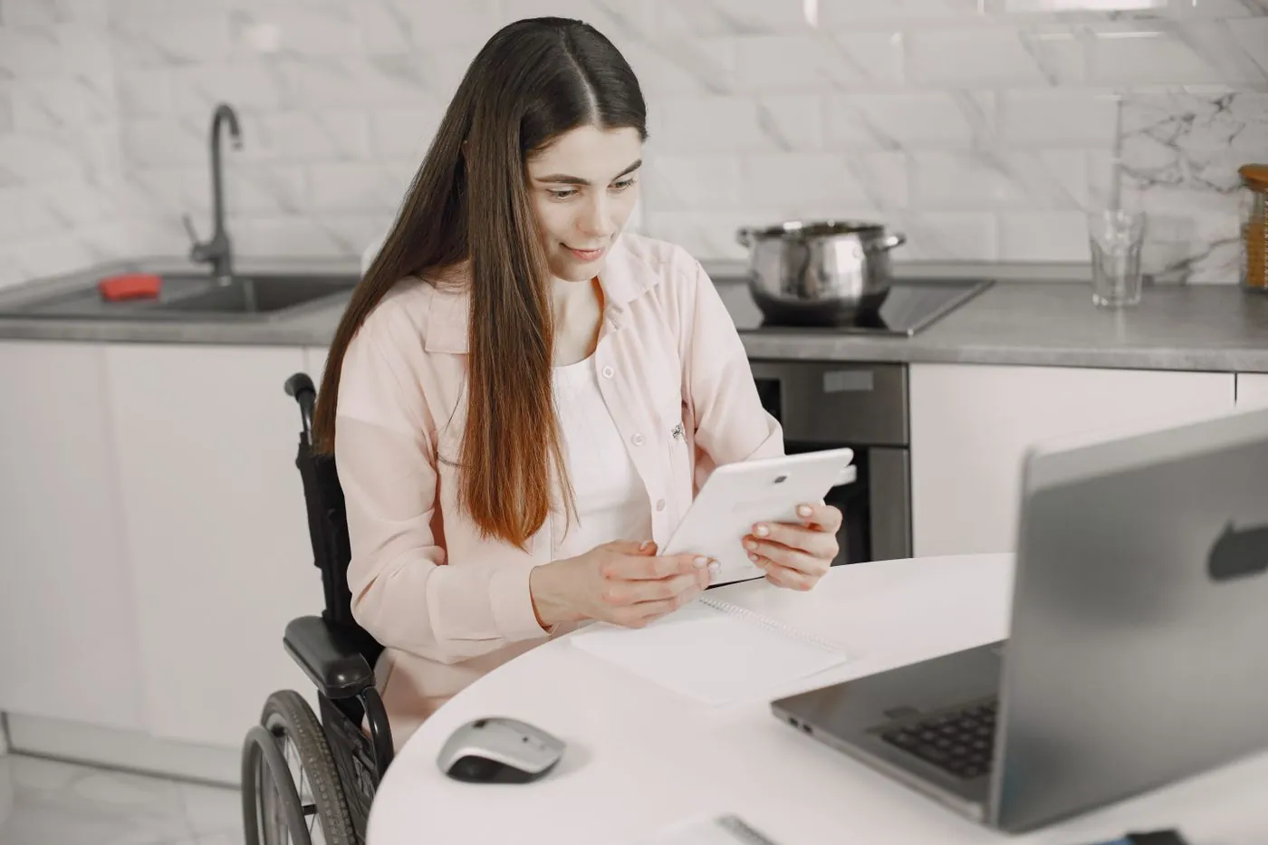 Žena na vozíku pracuje s tabletem u kuchyňského stolu
