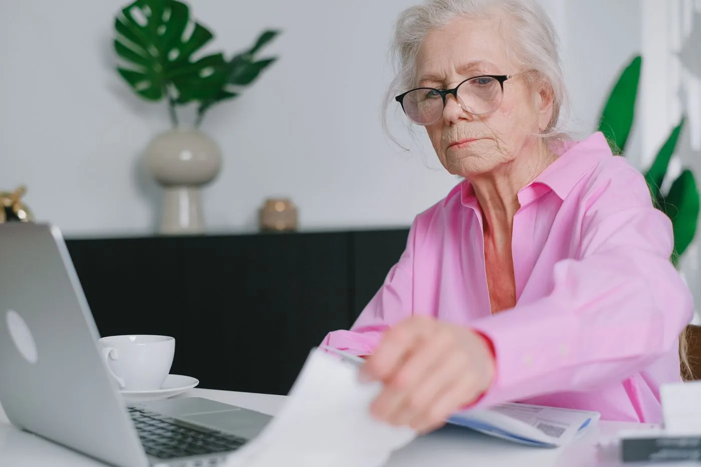 seniorka s brýlemi pracuje s laptopem a papíry
