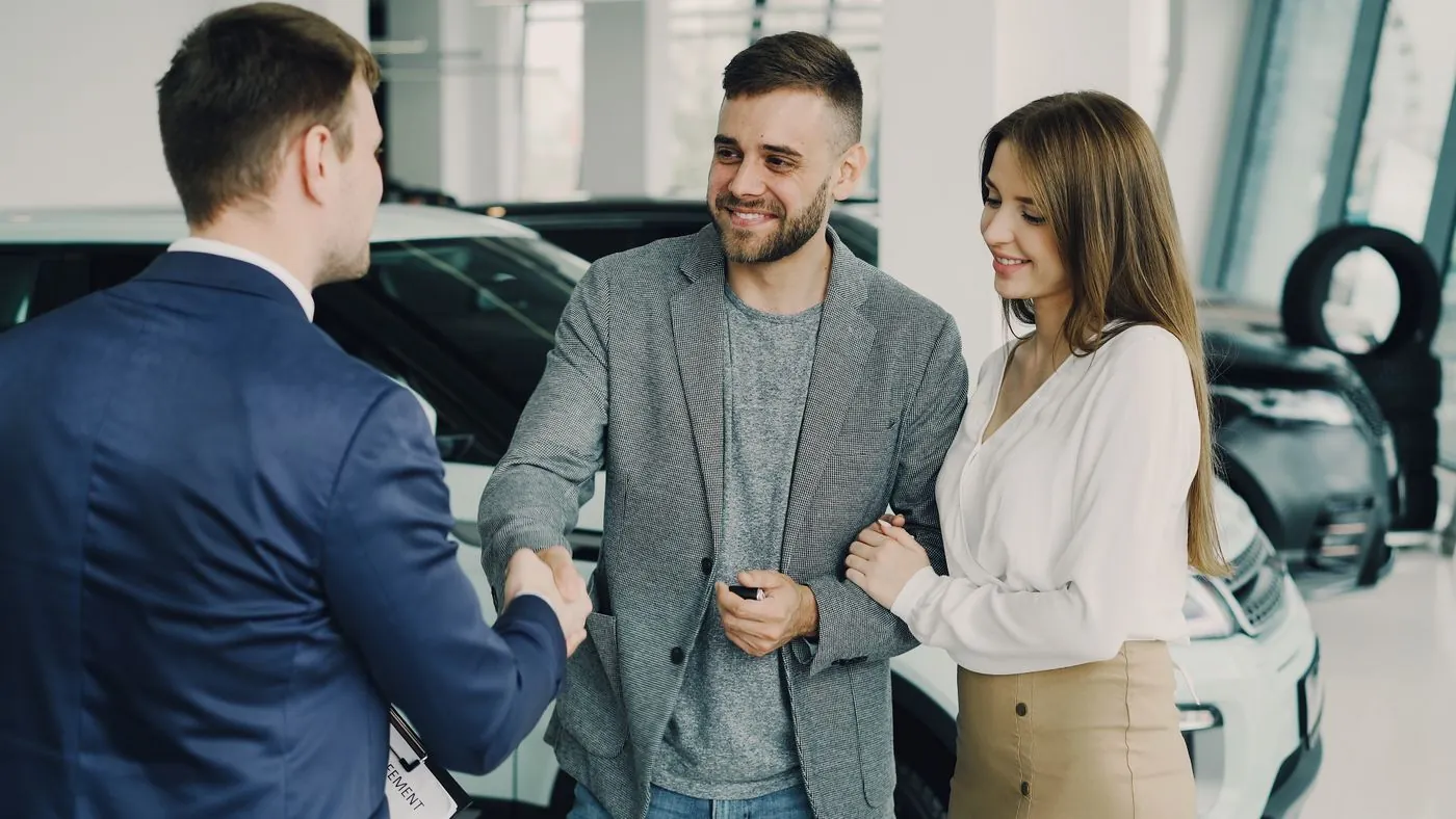 Prodejce podává ruku spokojenému páru v autosalonu
