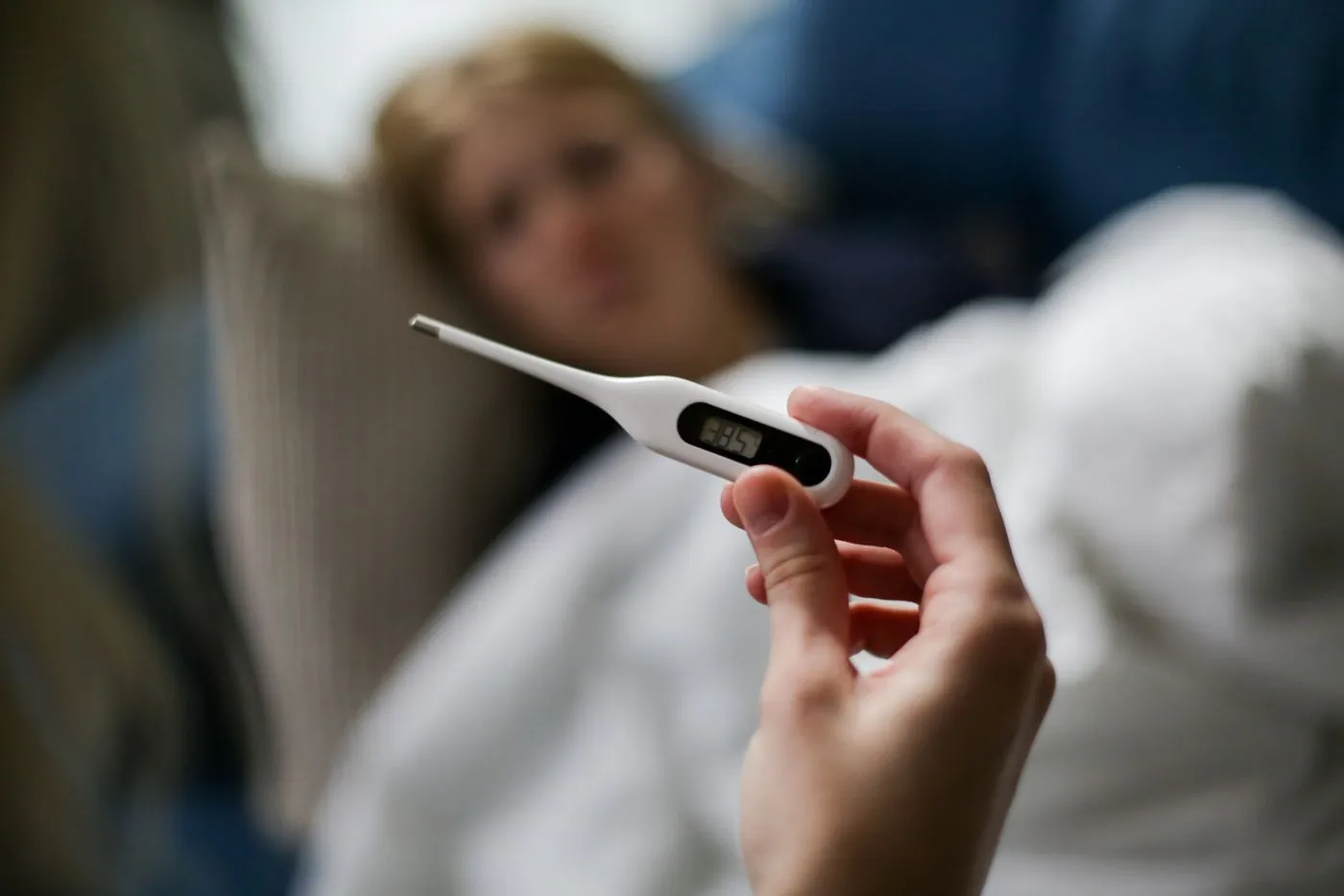 Ruka drží digitální teploměr u nemocného člověka v posteli